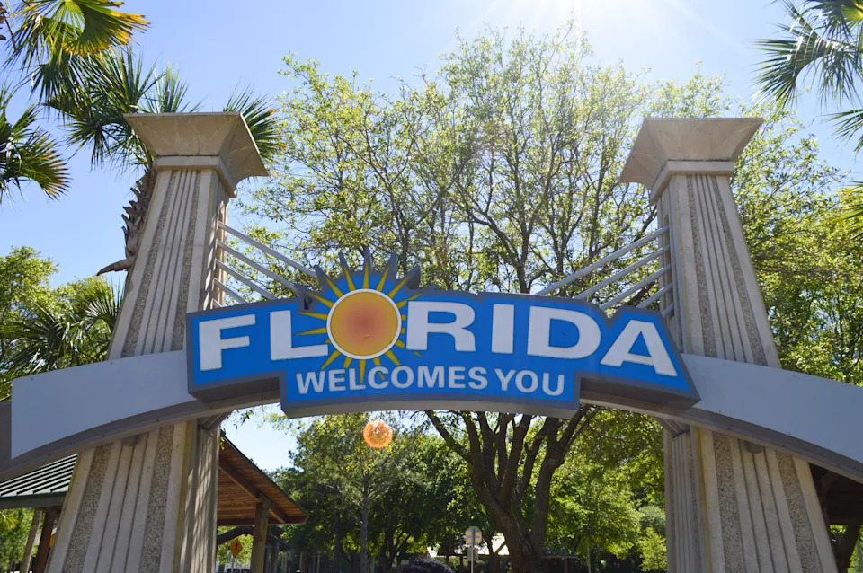 Florida welcome sign with large columns and a sun emblem, set amidst trees