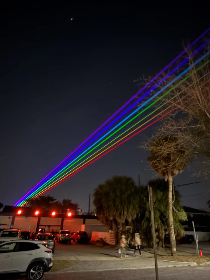 Six parallel lines in red, orange, yellow, green, blue, violet, and purple, shine across the sky of St. Petersburg, Florida