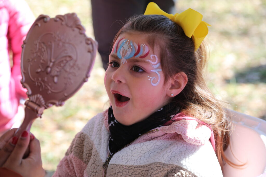 Girl with mouth open in excitement seeing her face-painted at Walk for Victory. 
