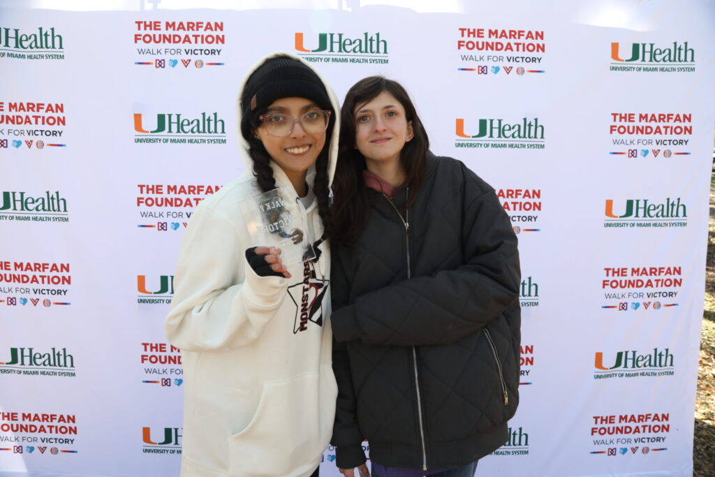 Two young women at the walk in front of the University of Miami Health logo sign .