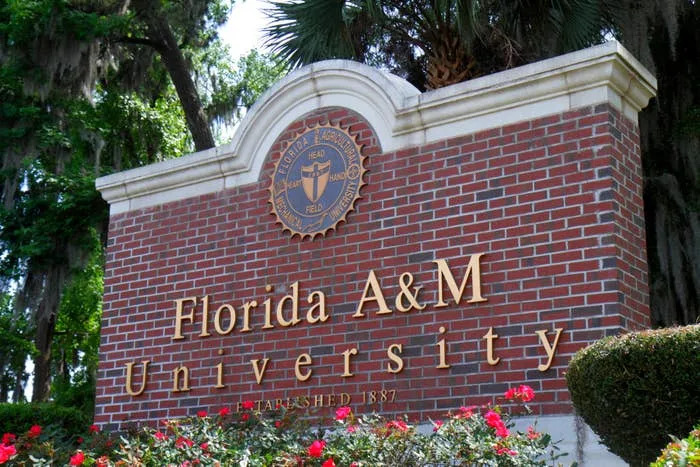 Brick sign for Florida A&M University with its seal and "Established 1887" inscription, surrounded by blooming flowers and trees