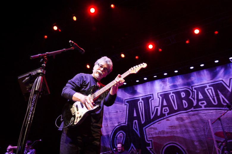 Randy Owen, lead singer of the country band Alabama, performing live on stage with a black electric guitar during a concert.
