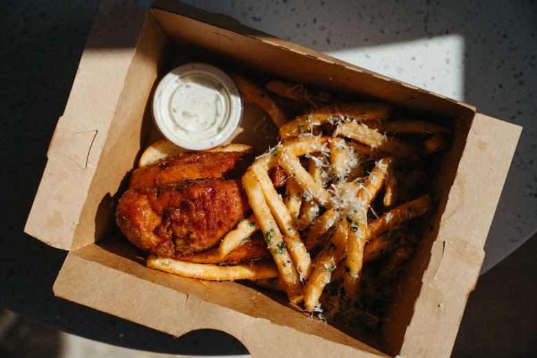 Crispy fried chicken and parmesan-dusted fries in a cardboard takeout box from Chicken and Pig at Depot 303 food hall in Mulberry, Florida.