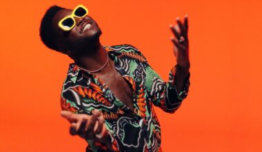 A man wearing yellow glasses and a colorful shirt against an orange background