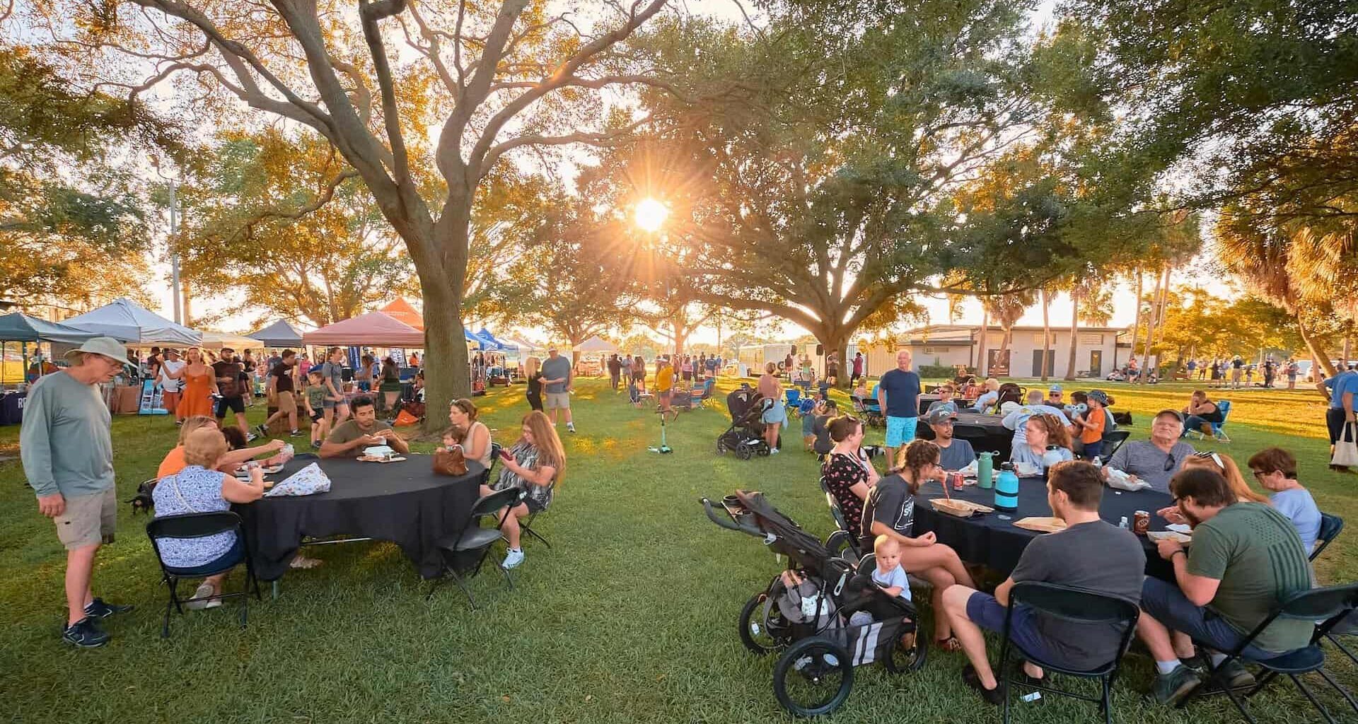 people eat and drink at picnic tables at a local park