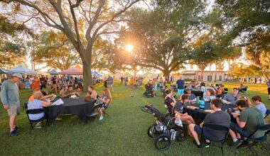 people eat and drink at picnic tables at a local park