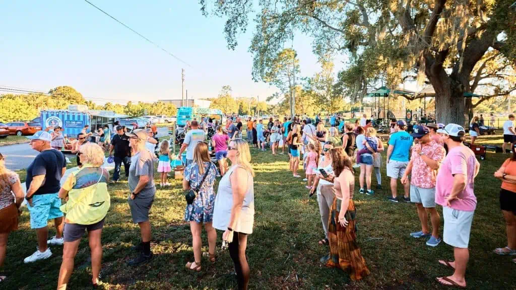 people gather around a row of food trucks at a local park