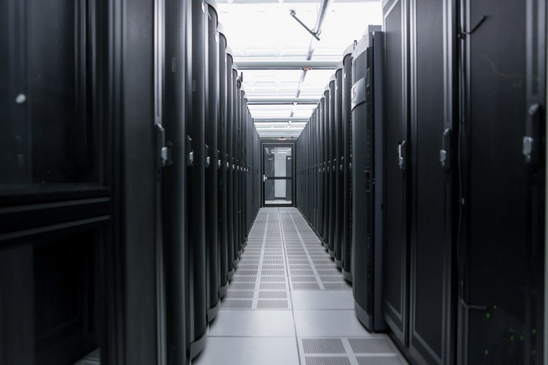 A long, symmetrical aisle lined with black server racks inside a modern data center facility.