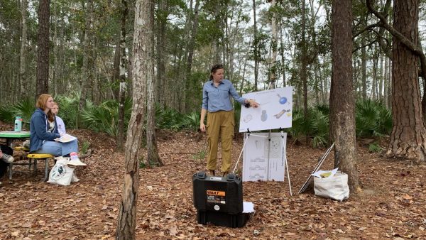 Woman points to white board set up in a forest.