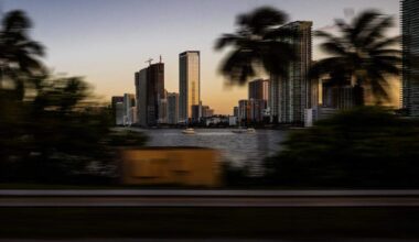 Miami Bayside buildings and skyline with palm trees blurred by motion at the end of the day, photographed from a car on the Miami Beach bridge in Miami, Florida.