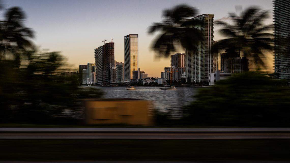 Miami Bayside buildings and skyline with palm trees blurred by motion at the end of the day, photographed from a car on the Miami Beach bridge in Miami, Florida.
