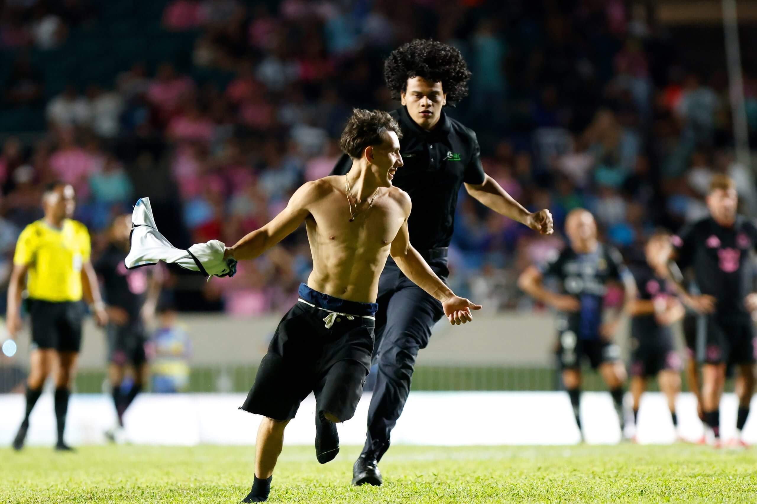 A security guard chases a fan who had run onto the pitch to greet Lionel Messi