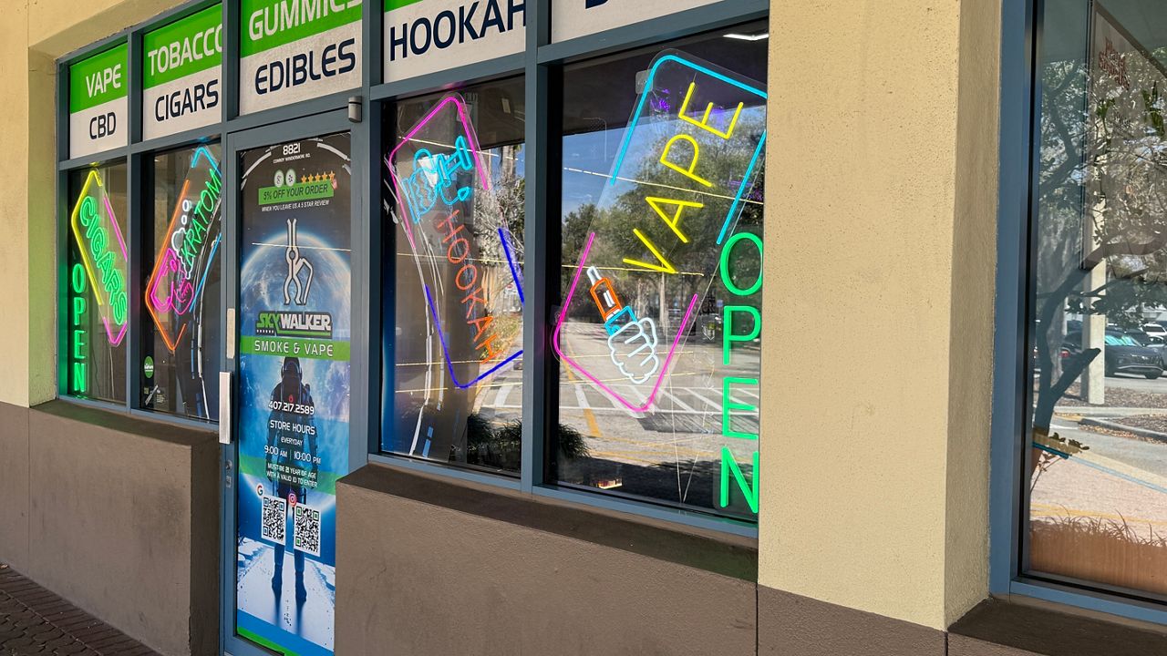 Neon signs and other signs in the store window of a store appear next to the sidewalk at a vape shop near Windermere.