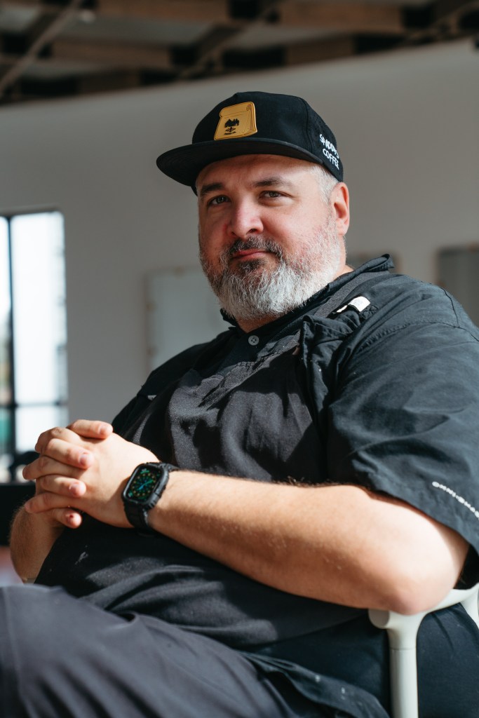 Portrait of Joe Dodd, owner of Chicken and Pig, wearing a black chef's shirt and hat at the Depot 303 food hall in Mulberry, Florida.