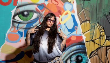 photo of a woman in a baggy shirt posing in front of a mural with painted eyes and splotches of paint