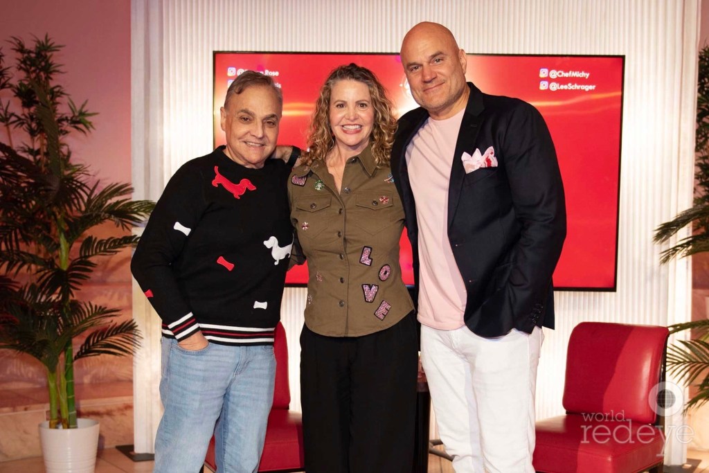 photo of three people — Lee Schrager, Michelle Bernstein, and Pablo Di Ritis — posing together in front of a red couch, wall frame, and plant