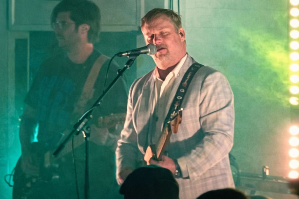 Photo of a man on stage playing the guitar and singing 
