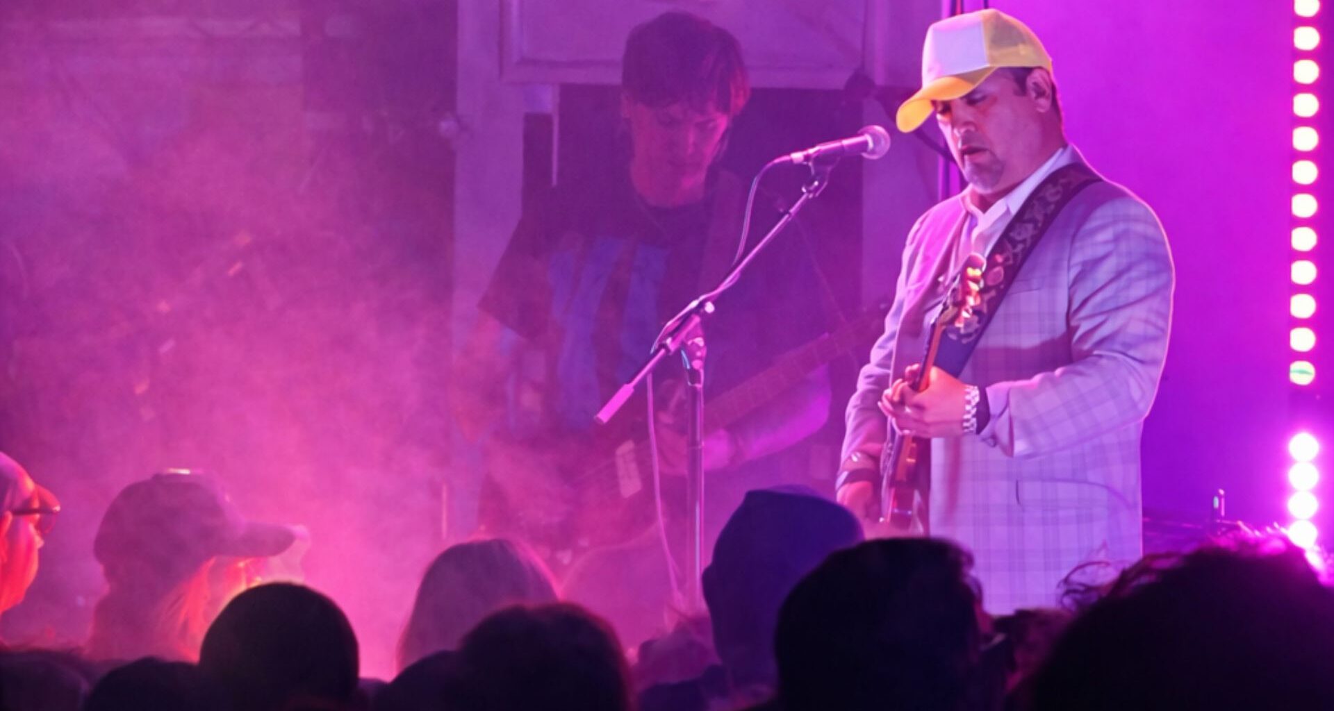 Photo of a band performing on stage under purple lights.