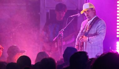 Photo of a band performing on stage under purple lights.