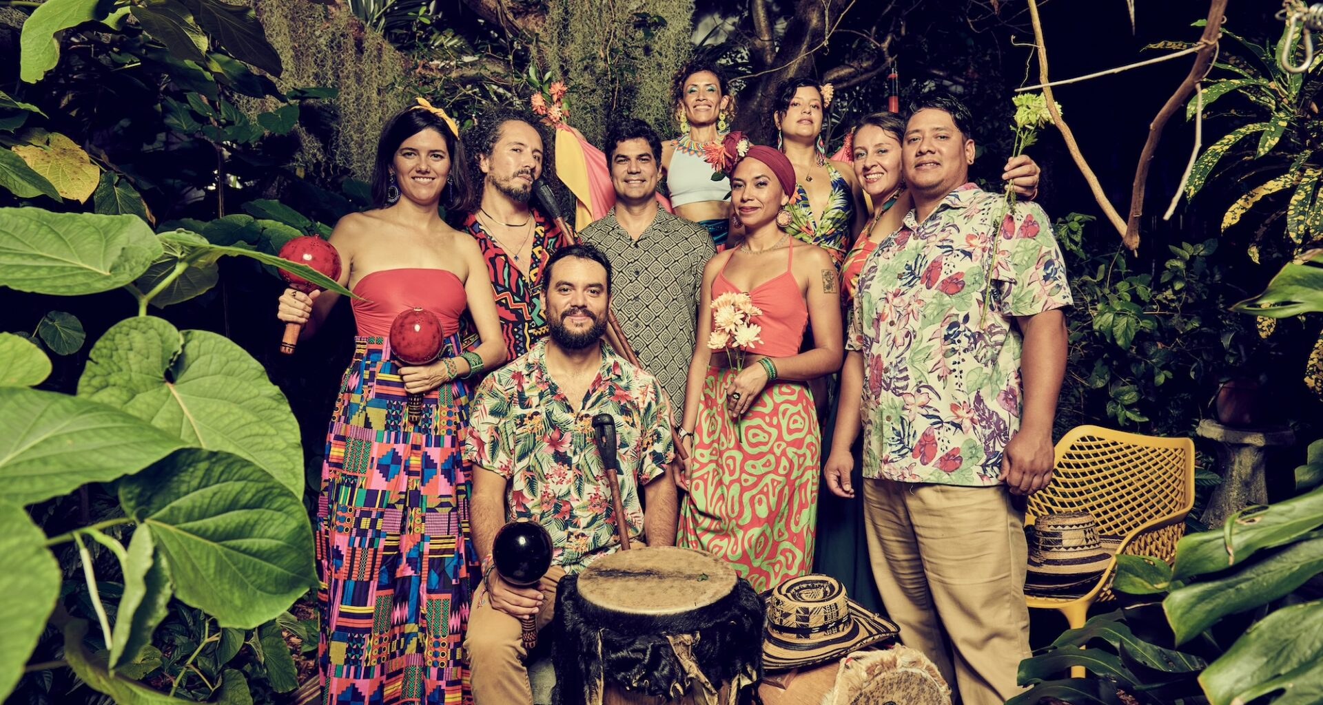 Photo of a band dressed in colorful colors posing in the middle of plants