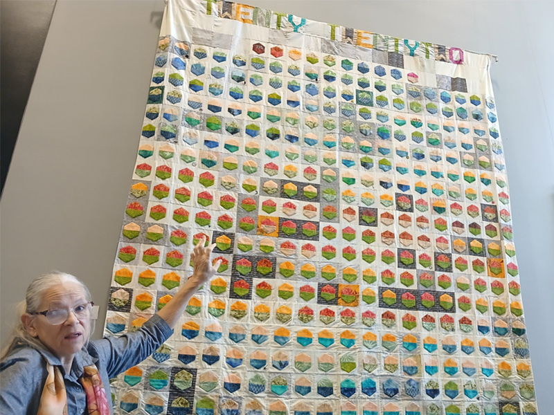 A woman displays a quilt showing weather data.