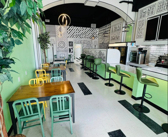 The interior of a cafe designed with a unique 2D comic book style, featuring black-and-white line art on the walls and bright green furniture.
