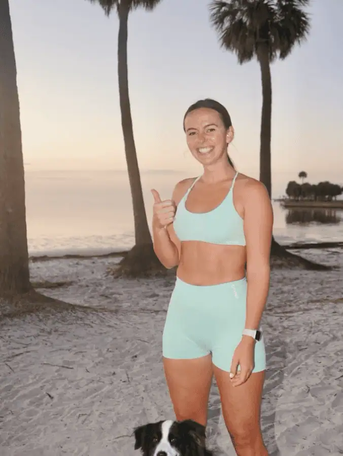 A woman gives a thumbs up and a smile with her dog on the beach