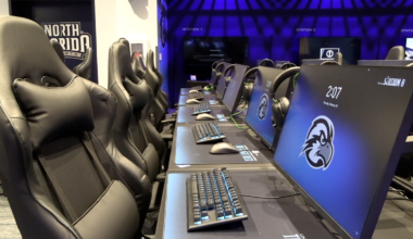 A room with 5 computers, black chairs and keyboards.