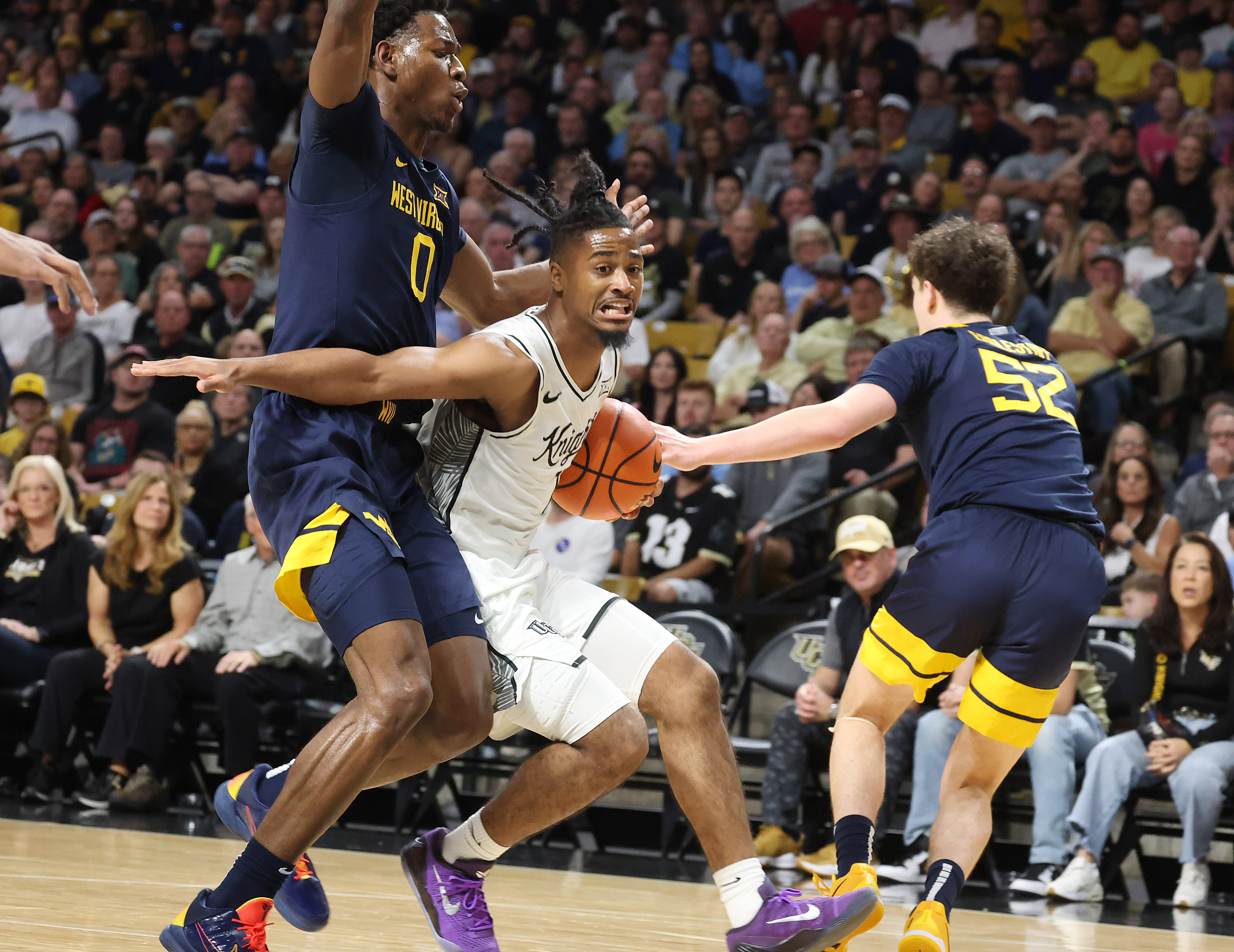 UCF guard Themus Fulks (middle) drives through West Virginia defenders...