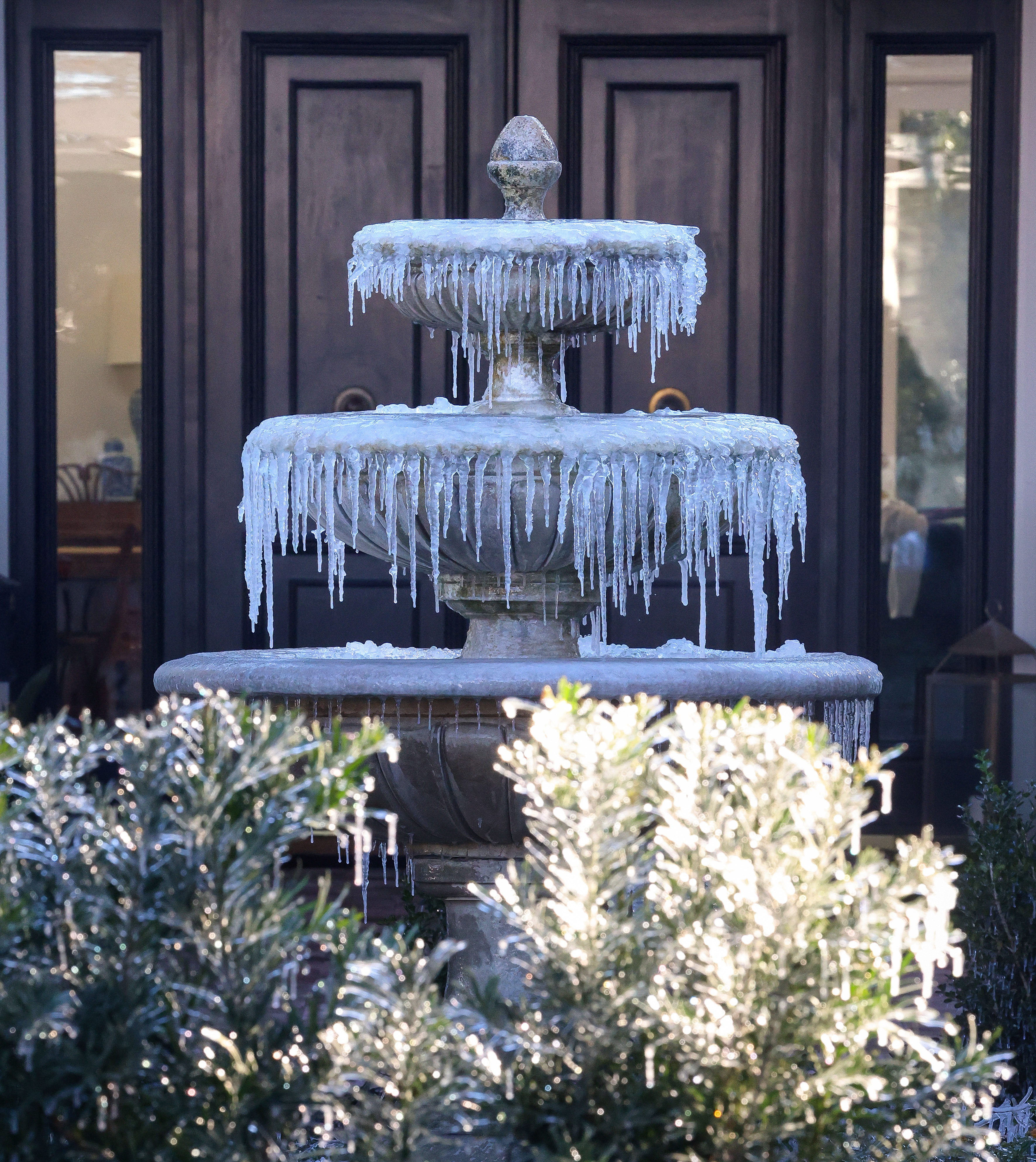 An iced-over fountain in front of a home in Winter...