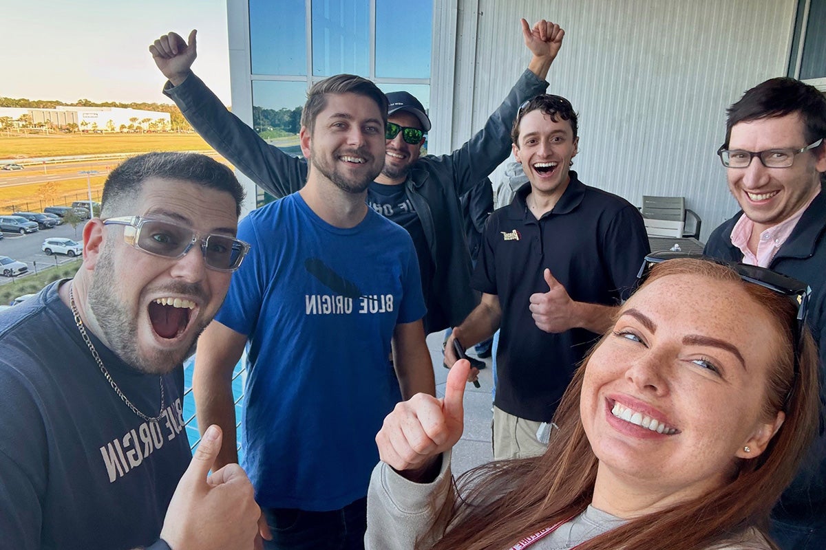 Five men and one woman smile as they take a selfie 