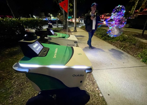 A balloon salesman passes robot delivery vehicles staged along on Wilton Drive in Wilton Manors on Friday, Feb. 7, 2026. (Amy Beth Bennett / South Florida Sun Sentinel)