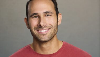 headshot of a smiling man wearing a red shirt in front of a gray background