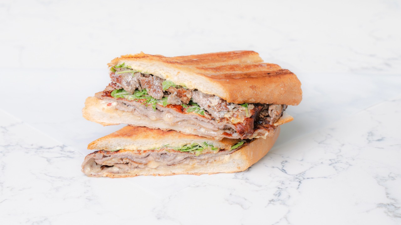 Bern’s Steak House and La Segunda Bakery steak sandwich, sliced in half on a white marble surface.