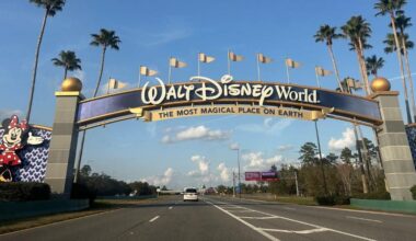 Entrance to Walt Disney World featuring a large archway with "The Most Magical Place on Earth" written below. Mickey and Minnie Mouse are displayed on pillars. Palm trees line the road under a blue sky.