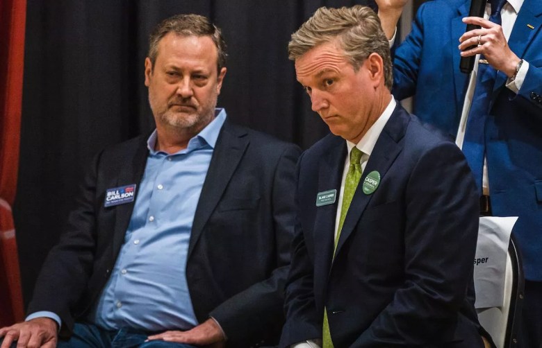 Tampa City Council District 4 candidates Bill Carlson and Blake Casper seated together at a 2023 election forum. Bill Carlson is on the left in a navy blazer; to his right, Blake Casper wears a dark suit with a green tie and a campaign button.