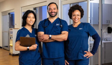 female, male and female nursing students wearing blue scurbs with their arms folded