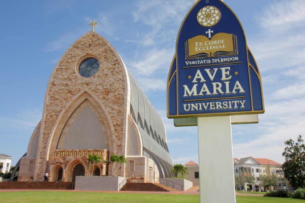 Sign for Ave Maria University in front of a Roman Catholic university building.