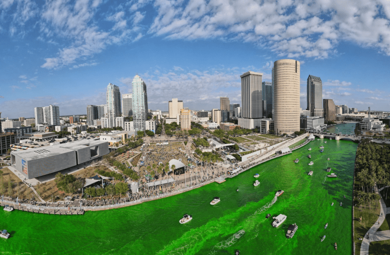 Aerial view of the Hillsborough River dyed bright green for the River O’ Green St. Patrick’s Day festival in downtown Tampa, featuring Curtis Hixon Waterfront Park and the city skyline.