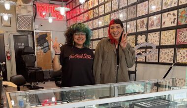 photo of two young women flashing the peace sign inside a tattoo studio with designs on the walls