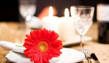 A gerbera daisy sits on a plate on a candle-lit table