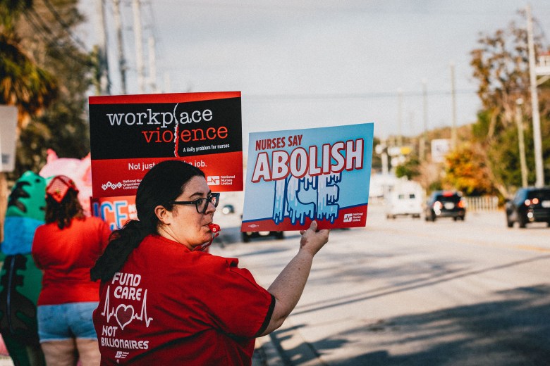 National Nurses United demonstrator blowing a whistle and holding 'Abolish ICE' and 'Workplace Violence' protest signs during a street rally.