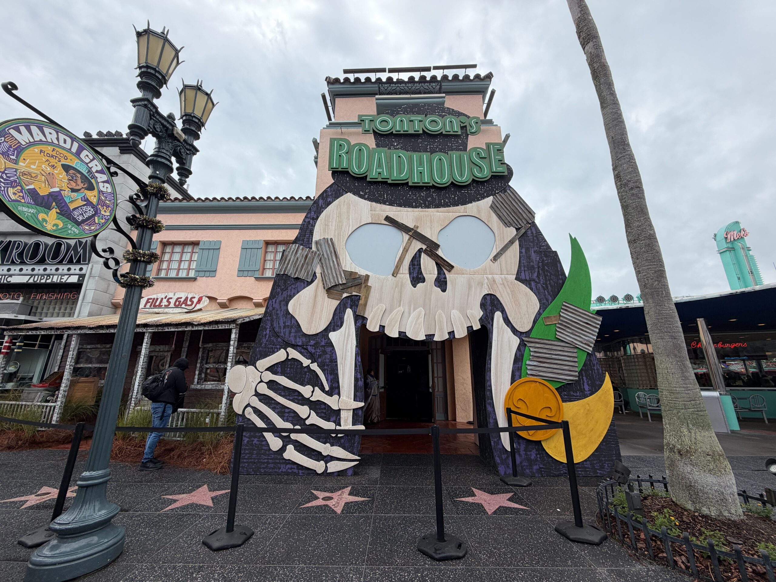 The theme of this year's store is "TonTon's Roadhouse," inspired by the event's mascot Baron TonTon. Guests enter through a large carnival-style skull face with corrugated paneling and a fleur-de-lys coin around it.
