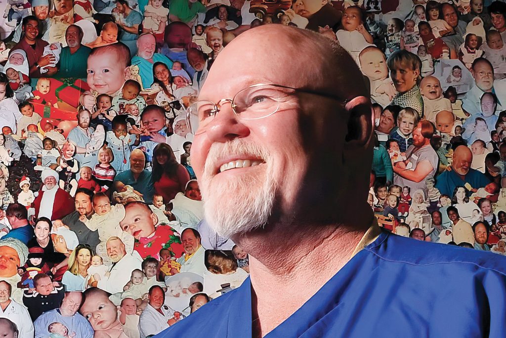Dr. Wade Barnes poses, prior to his retirement, before a wall of photos of the babies he delivered