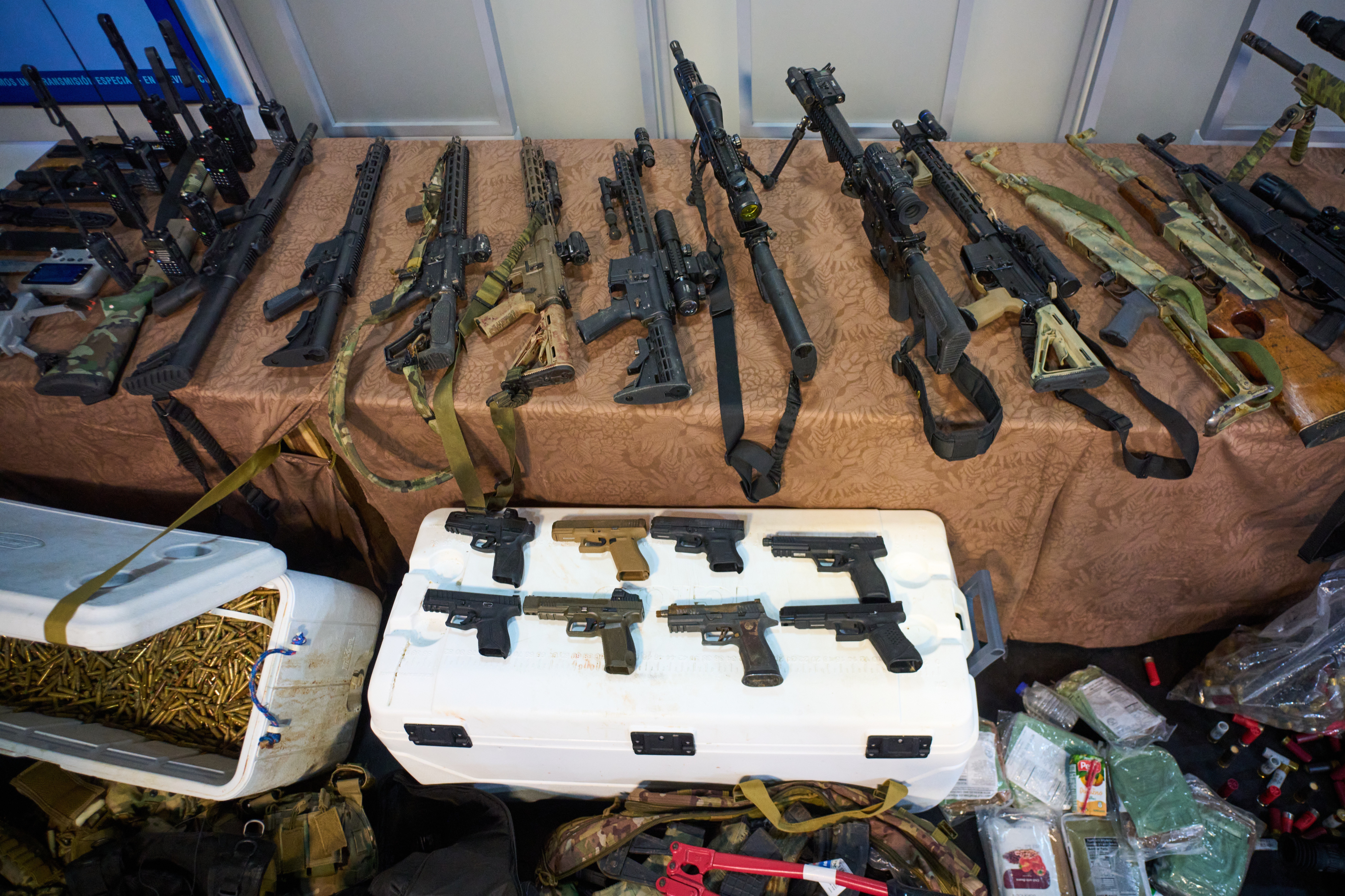 A collection of weapons and ammunition, including rifles, handguns, and walkie-talkies, displayed on a table.