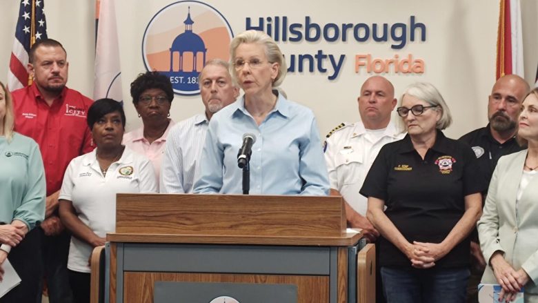 Tampa Mayor Jane Castor speaking at a podium during a Hillsborough County, Florida press conference, flanked by local officials and first responders.