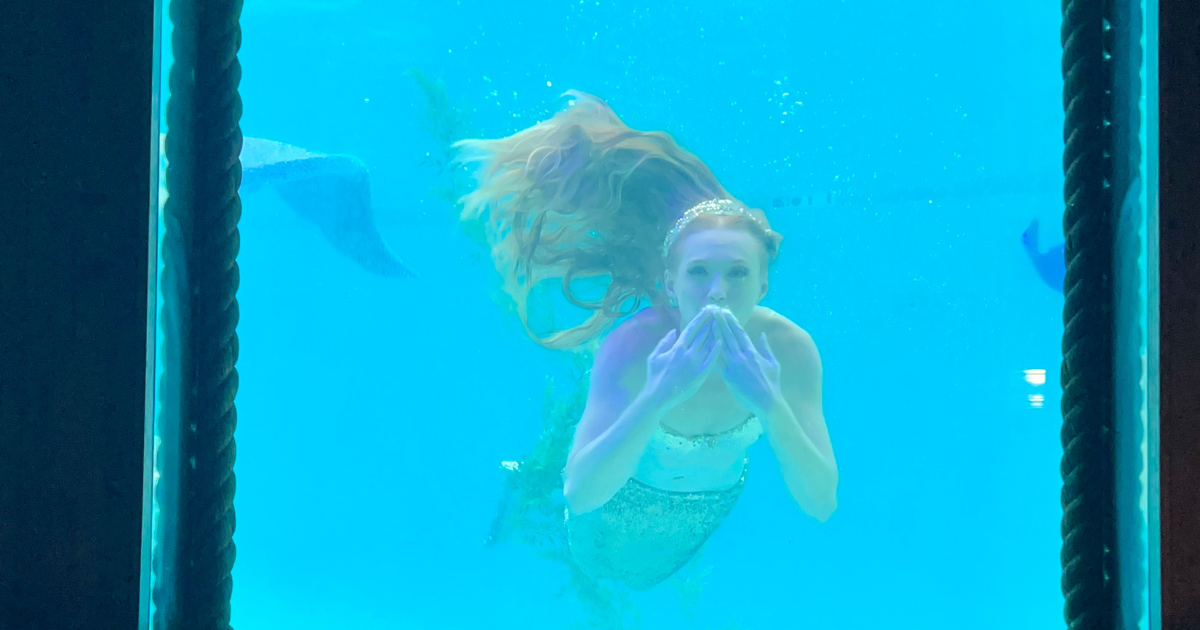 Professional mermaid performer at The Wreck Bar Fort Lauderdale blowing a kiss through a porthole window.