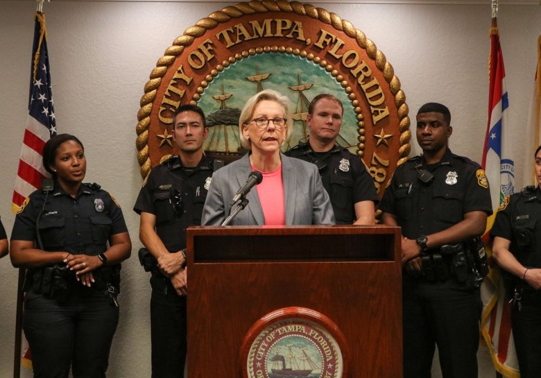 Tampa Mayor Jane Castor speaking at a podium during a press conference, flanked by five Tampa Police Department officers in uniform in front of the City of Tampa Florida seal.