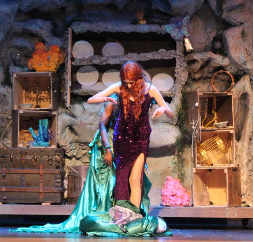 Katt Torres as Ariel steps out of outer garment to reveal purple gown she's wearing underneath.