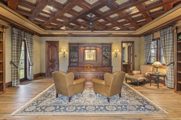 The formal office is separate from the main house and connected by a covered walkway. It has a wood coffered ceiling and multiple built-in bookshelves. (Photo by Michael Pelzer / Uneek Luxury)